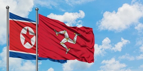 North Korea and Isle Of Man flag waving in the wind against white cloudy blue sky together. Diplomacy concept, international relations.