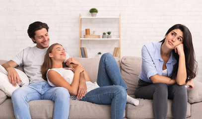 Bored Girl Sitting With Friends Hugging On Couch At Home