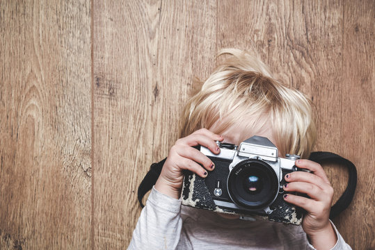 Boy taking a photo with a vintage camera learning at home how to take a picture the child is holding camera with both hands and pointing lens at the viewer