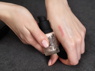 Woman's beauty blogger hands applies sample liquid tone base color on skin with copyspace