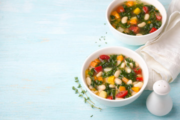 Vegan bean soup with vegetables and kale cabbage in white bowls on blue background, free space, horizontal