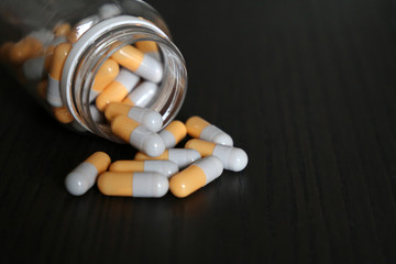 Capsules on a dark wooden table, medication in pills scattered from a bottle. Concept of pharmacy, antibiotics, vitamins