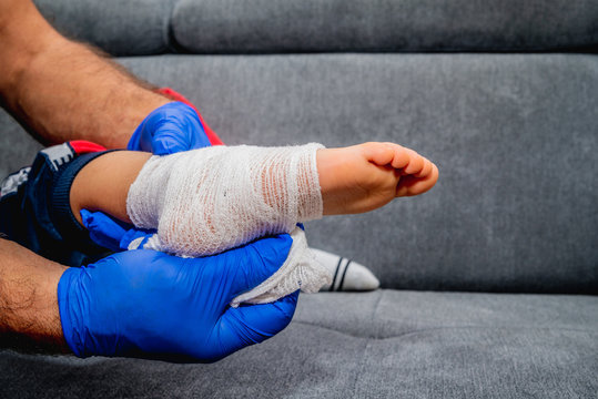 Bandaging Of The Child's Foot. Health And Pharmaceutical Concept, Child Health Problems. The Doctor Bandages And Stiffens The Child's Foot, Ankle. Sprain Or Fracture Of The Leg.