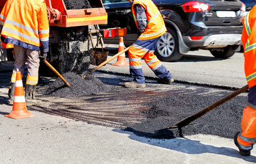Working team levels the fresh asphalt with shovels on a repaired area in road construction.