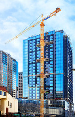 Fototapeta na wymiar The glass facade, a reflection of the blue sky and crane near a modern concrete building under construction.
