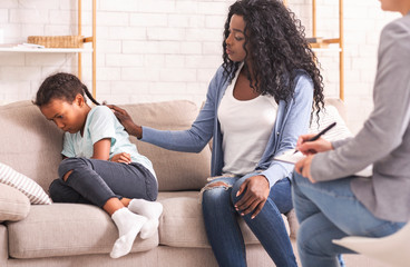 Mother soothing her upset disobedient little daughter at psychologist consultation