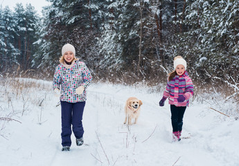 Fototapeta na wymiar mother and daughter running with white retriever dog in winter park. Cute young family fun in winter park with their dog golden retriever on a sunny day and smiling. Winter activities for family with 