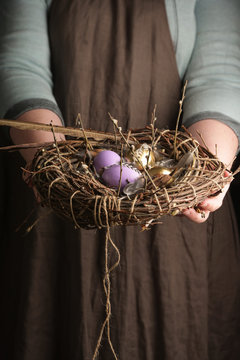 Woman holding a in hand nest with colored eggs and feathers for Easter. Rustic style. Vertical.