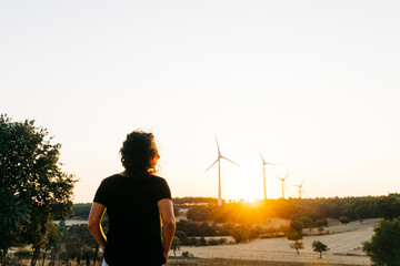 A female model who is wearing black basic t-shirt and at back ground renewable energy wind turbines on the mountain at sunset time