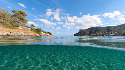 Above and below underwater photo of tropical exotic turquoise sandy beach in Caribbean secluded destination with deep blue sky and clouds