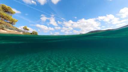 Fototapeta na wymiar Above and below underwater photo of tropical exotic turquoise sandy beach in Caribbean secluded destination with deep blue sky and clouds