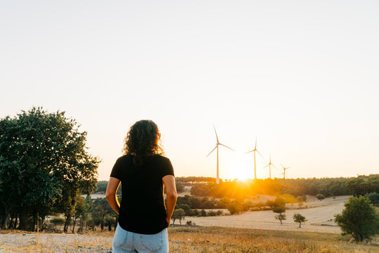 A female model who is wearing black basic t-shirt and at back ground renewable energy wind turbines on the mountain at sunset time