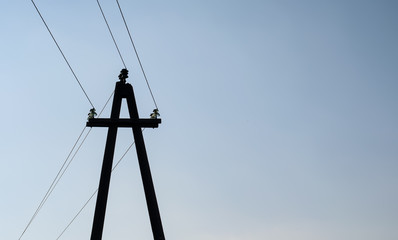 Dark silhouette of concrete utility pole with insulators and high voltage wires, blue sky...