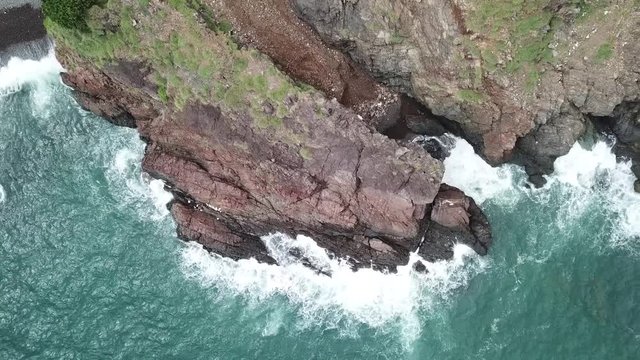 A flying camera takes a motorcyclist passing on a road near the sea with a view of the rocky shore.
