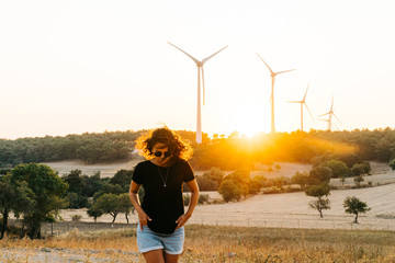 A female model who is wearing black basic t-shirt and at back ground renewable energy wind turbines on the mountain at sunset time