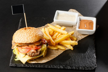 Big single cheeseburger with french fries isolated on black background. hamburger with beef patty , onion, tomato, lettuce pickles, aged cheddar, mustards, tomato jam, mayo. Horizontal