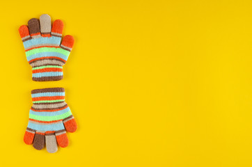 Striped kids winted gloves composition on yellow background.