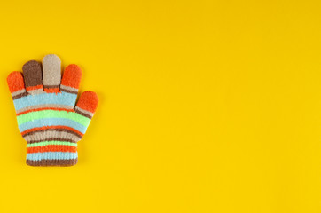 Striped kids winted gloves composition on yellow background.