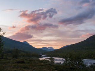Wild Tjaktjajakka river and Kaitumjaure lake with waterfall cascade and mountains. Lapland nature landscape in summer, sunset pink clouds