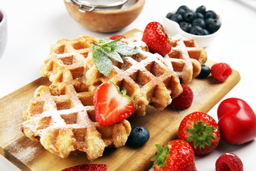 Traditional belgian waffles with fresh blueberries, sugar and raspberries on rustic table