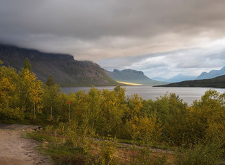 Beatiful golden light sunrise at river Lulealven in Saltoluokta in Sweden Lapland. Green rocky mountain, birch trees and clouds.