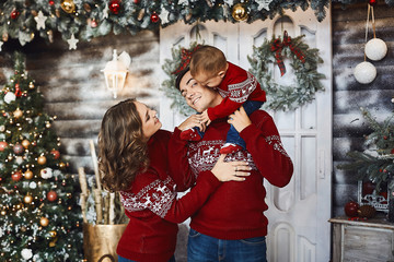 Beautiful couple with their cute little son in the same fashionable winter clothes. Mom, Dad and their son hugs together and have fun in the Christmas interior. Family holidays. Happy New year.