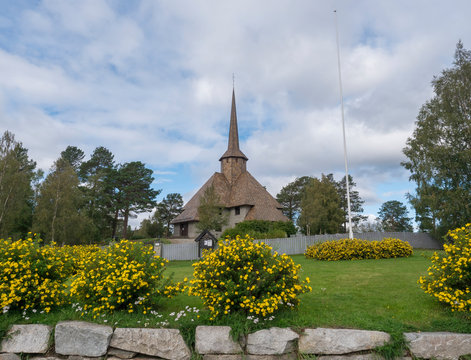 The old church of Dombas in traditional style with blooming yellow flowers. Blue sky, white cloud background. Oppland, Norway