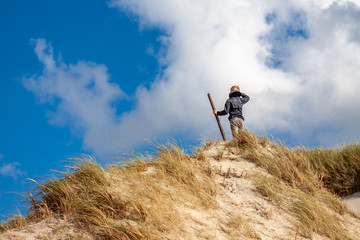 Young boy with stick standing on top of sand dune