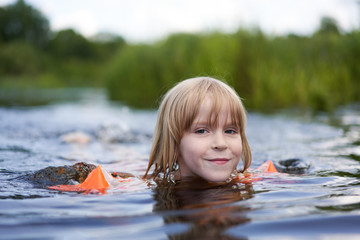Girl clumsily swims in a small pond near the shore.
