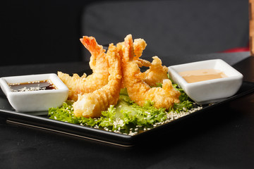 Tempura Deep Fried Shrimp Ebi with sweet chili and soy sauce on black board stone on dark background. Japanese food style appetizer. Deep fried prawn in breeding close up. Horizontal photo.