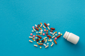 A handful of colored pills spilled out of the can on a blue background. Medical concept