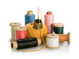 Group of old coils with multi-colored threads and needle with thimble from brass