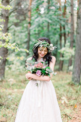 Fototapeta na wymiar stylish young smiling bride holding rustic bouquet of amazing flowers, posing in pine forest outdoors
