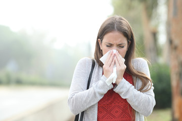 Ill woman blowing using tissue walking in a park with fog