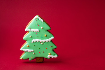 gingerbread cookie of green Christmas Tree on red background. Traditional Christmas food. Christmas and New Year holiday concept. Copyspace