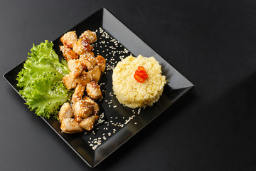 Chicken with sweet and sour sauce. Fried chicken pieces in batter with sweet and sour sauce. Chinese chicken sweet and sour sauce, served with ouscous and vegetables on dark background. Horizontal.