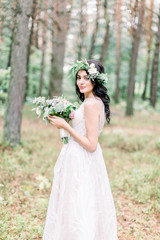 Obraz na płótnie Canvas Beautiful bride with bouquet of flowers in white dress stands on forest background. Rustic style