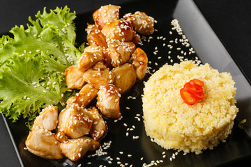 Chicken with sweet and sour sauce. Fried chicken pieces in batter with sweet and sour sauce. Chinese chicken sweet and sour sauce, served with ouscous and vegetables on dark background. Horizontal.
