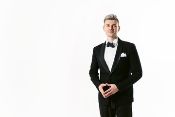 Portrait of young smiling handsome man in tuxedo stylish black suit, studio shot isolated on white background. Showman or toastmaster in jacket with bowtie