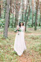 Full-length view of the smiling bride in the wedding dress walking in the green forest.