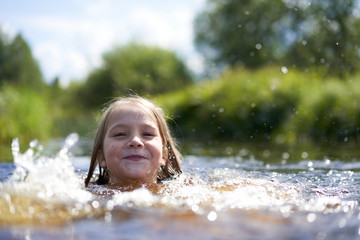 Girl clumsily swims in a small pond near the shore.