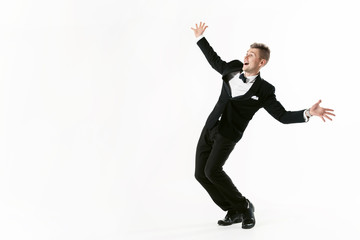 Portrait of young smiling handsome show man in tuxedo stylish black suit, studio shot dancing at white background. Businessman in jacket with bowtie