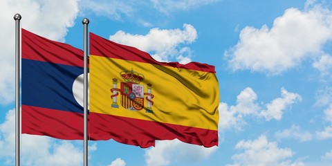 Laos and Spain flag waving in the wind against white cloudy blue sky together. Diplomacy concept, international relations.