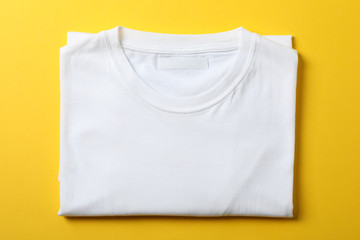 Folded blank white t-shirt on yellow background, space for text