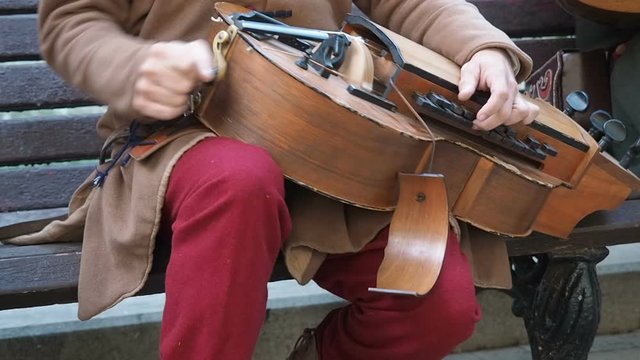 Street musician dressed in vintage ethnic oriental clothes play music on traditional Middle Eastern musical instrument hurdy-gurdy also named wheel fiddle, wheel vielle