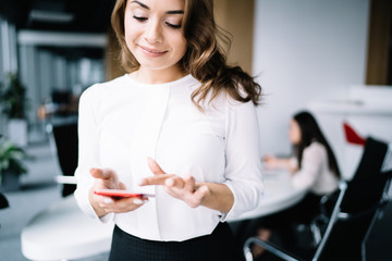 Cheerful woman browsing smartphone at workplace