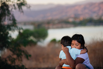 Brother and sister separated from parents are hugging each other in a foreign country, across a...