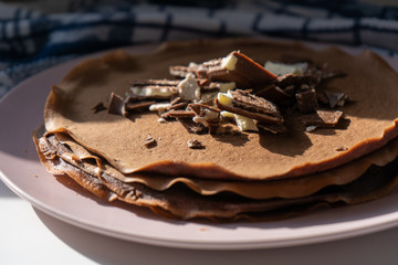 Close-up. Сhocolate pancakes with chocolate and waffles on a pink plate in the morning and blue towel on the wooden background. Side view