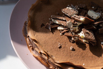 Close-up. Сhocolate pancakes with chocolate and waffles on a pink plate in the morning and blue towel on the wooden background.