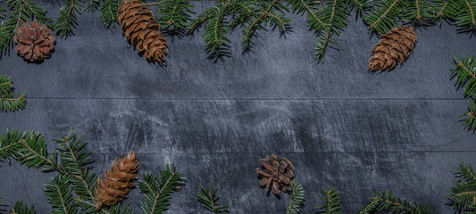 Frame of natural fir pine branches and cones on rustic dark black grey wooden table - christmas...